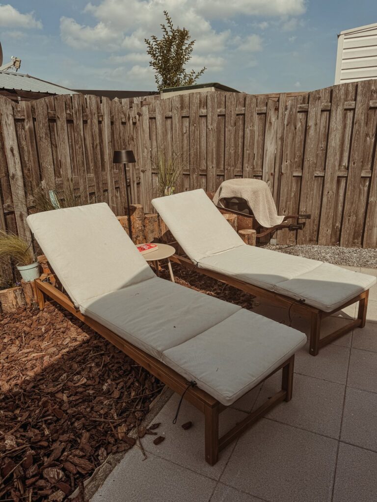 Twee houten ligbedden met crème kussens op het terras