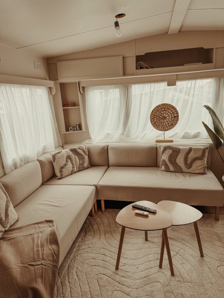 Woonkamer van de stacaravan met beige hoekbank en houten salontafels