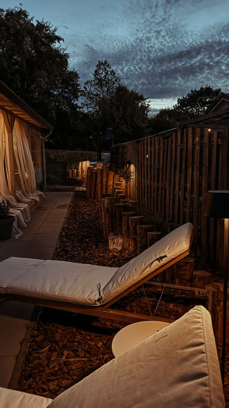 Tuin van Slow Nest in de avondschemering met loungers en lantaarnlicht, aan de Oosterschelde